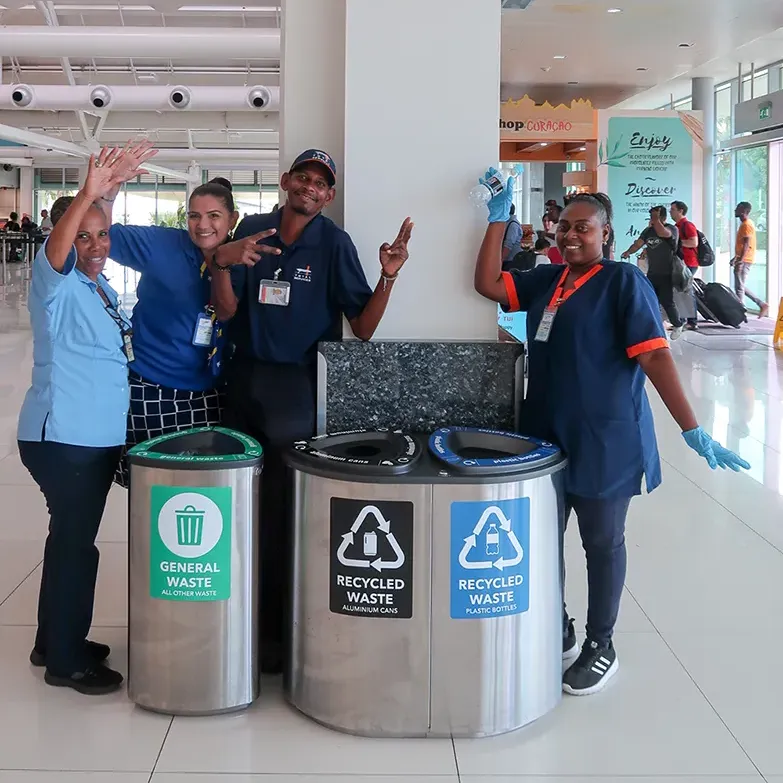 Four people at the airport of Curacao standing next to new recycling bins